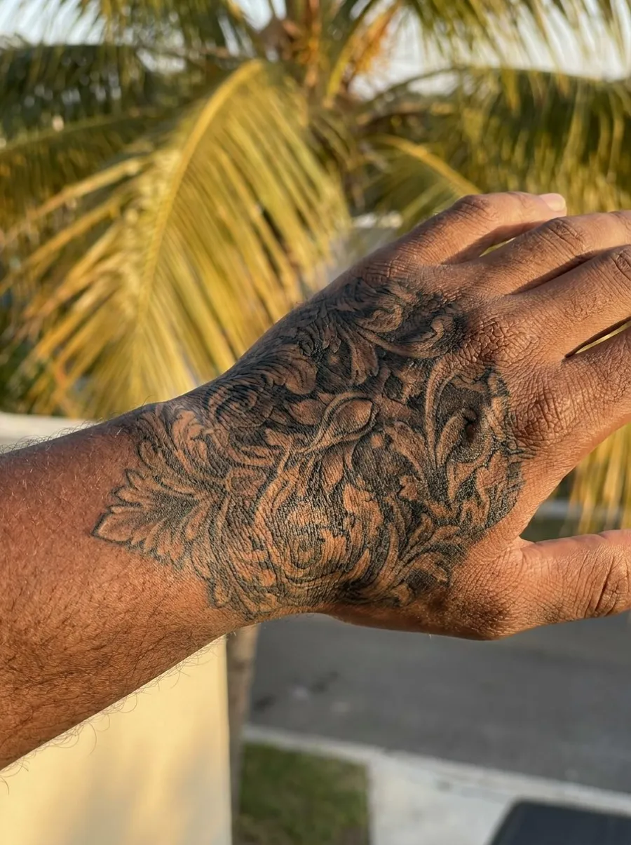 Tatouage manchette black & grey ornementale du poignet à la main, motifs gothiques et floraux sur peau mate, lumière naturelle extérieure