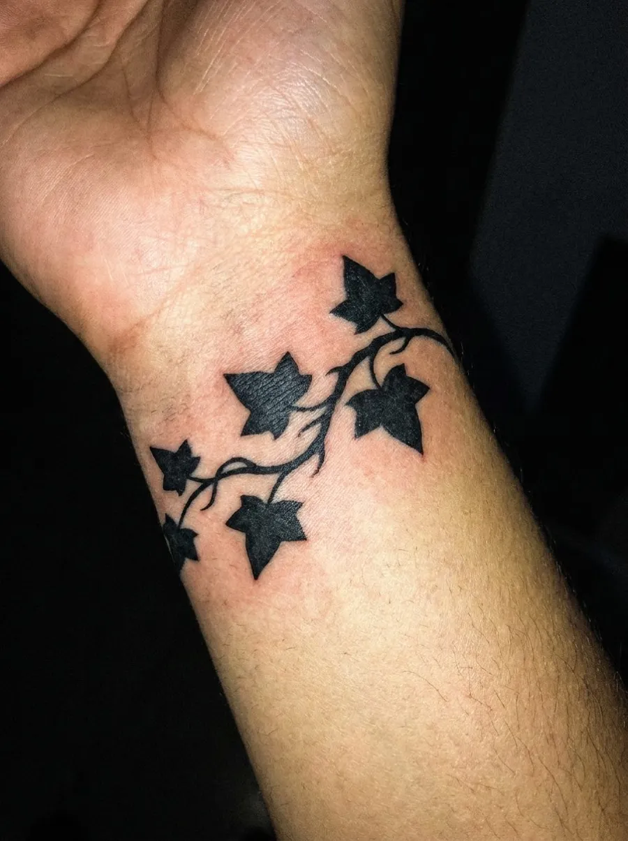 Tatouage blackwork représentant une branche de lierre stylisée enroulée autour du poignet, feuilles en silhouettes noires pleines aux contours nets