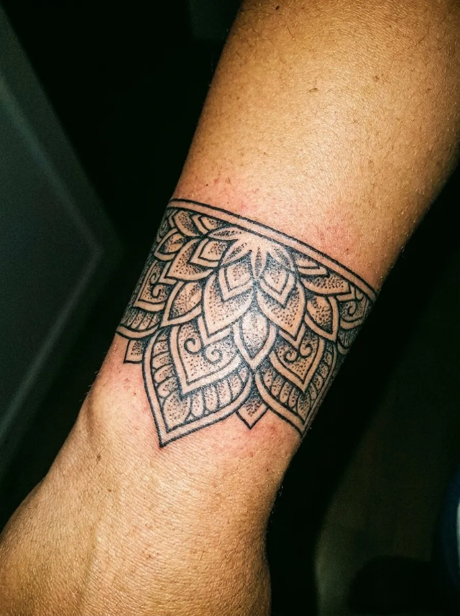 Tatouage bracelet ornemental mandala en blackwork avec motifs géométriques et dotwork enroulé autour de l'avant-bras près du poignet
