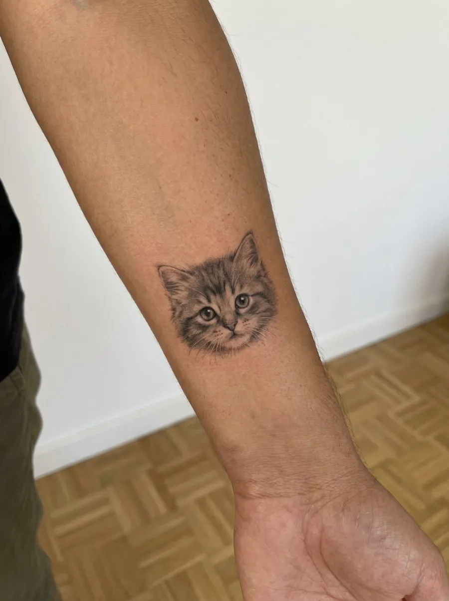 Tatouage microréaliste d'un chaton en noir et gris, 5 à 8 cm, posé sur l'avant-bras intérieur près du poignet, sur peau mate